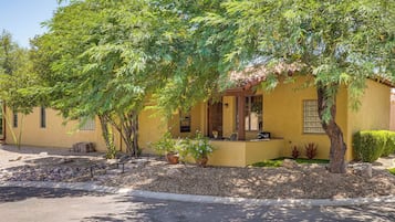 A yellow building with a porch, surrounded by trees and shrubs.