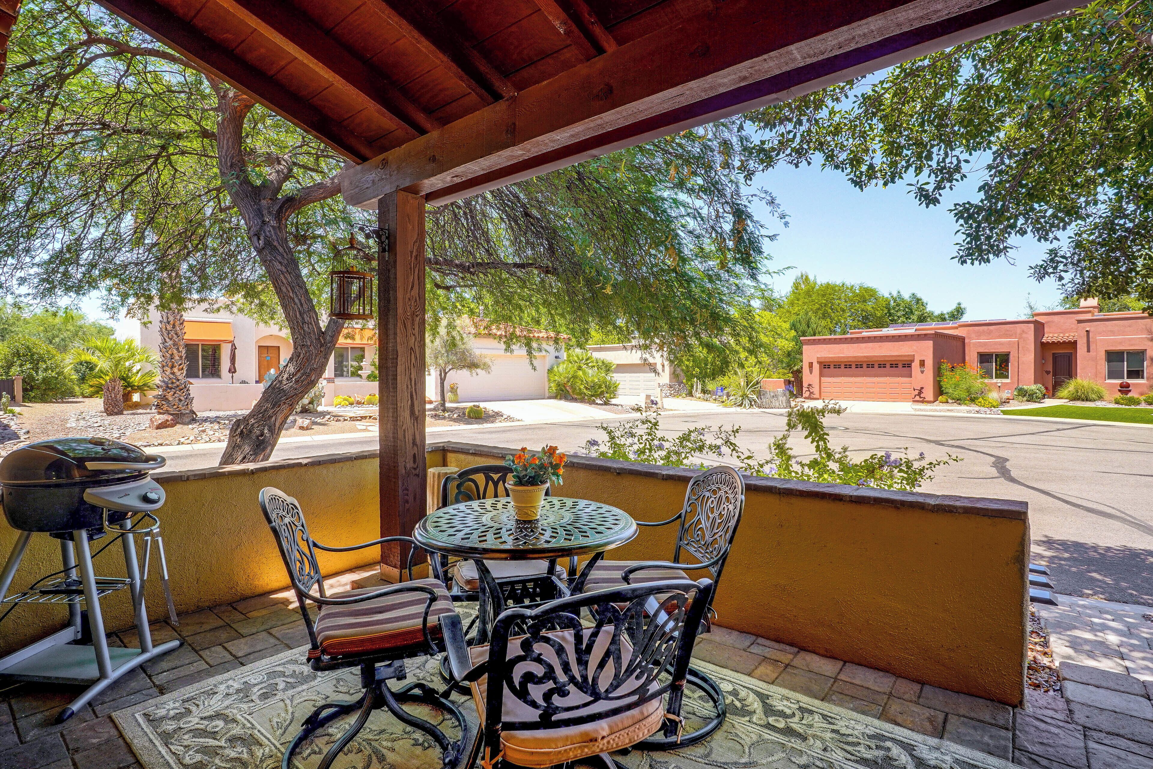 An outdoor patio with a round table and chairs, a grill, and a view of a residential area with houses and trees.