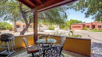An outdoor patio with a round table and chairs, a grill, and a view of a residential area with houses and trees.