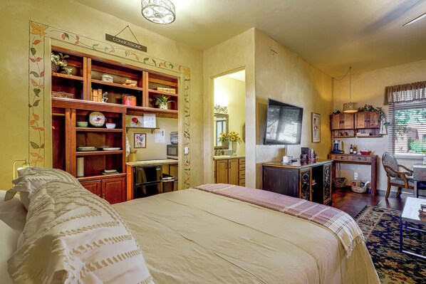 A hotel room with a bed, a desk, a kitchenette, and a bathroom.