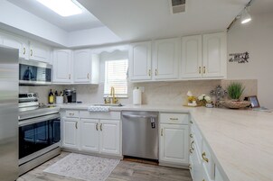 Cozinha moderna com armários brancos, eletrodomésticos de aço inoxidável e bancada de mármore.