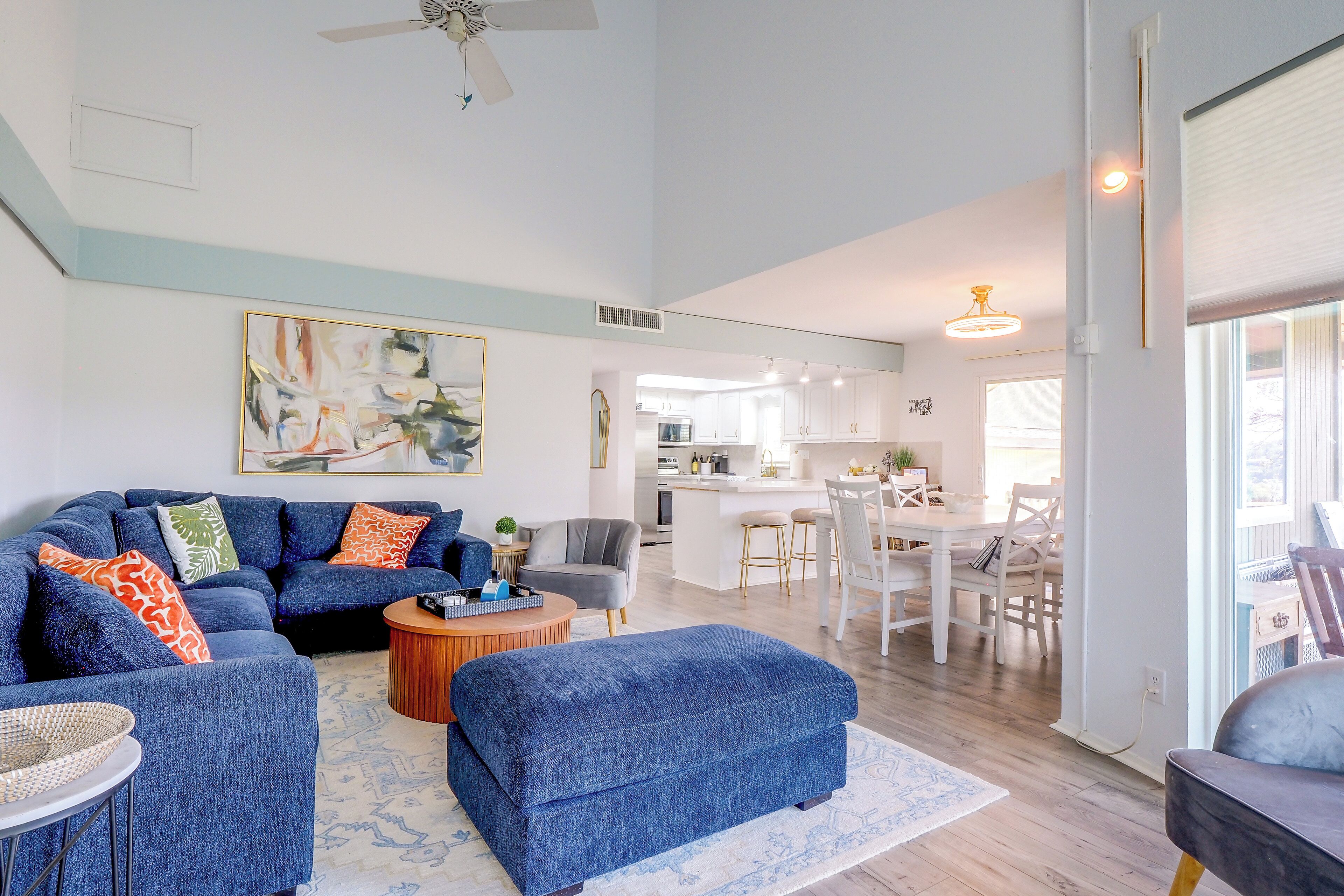 A spacious living room with a blue sofa set, a coffee table, and a dining area with white furniture.