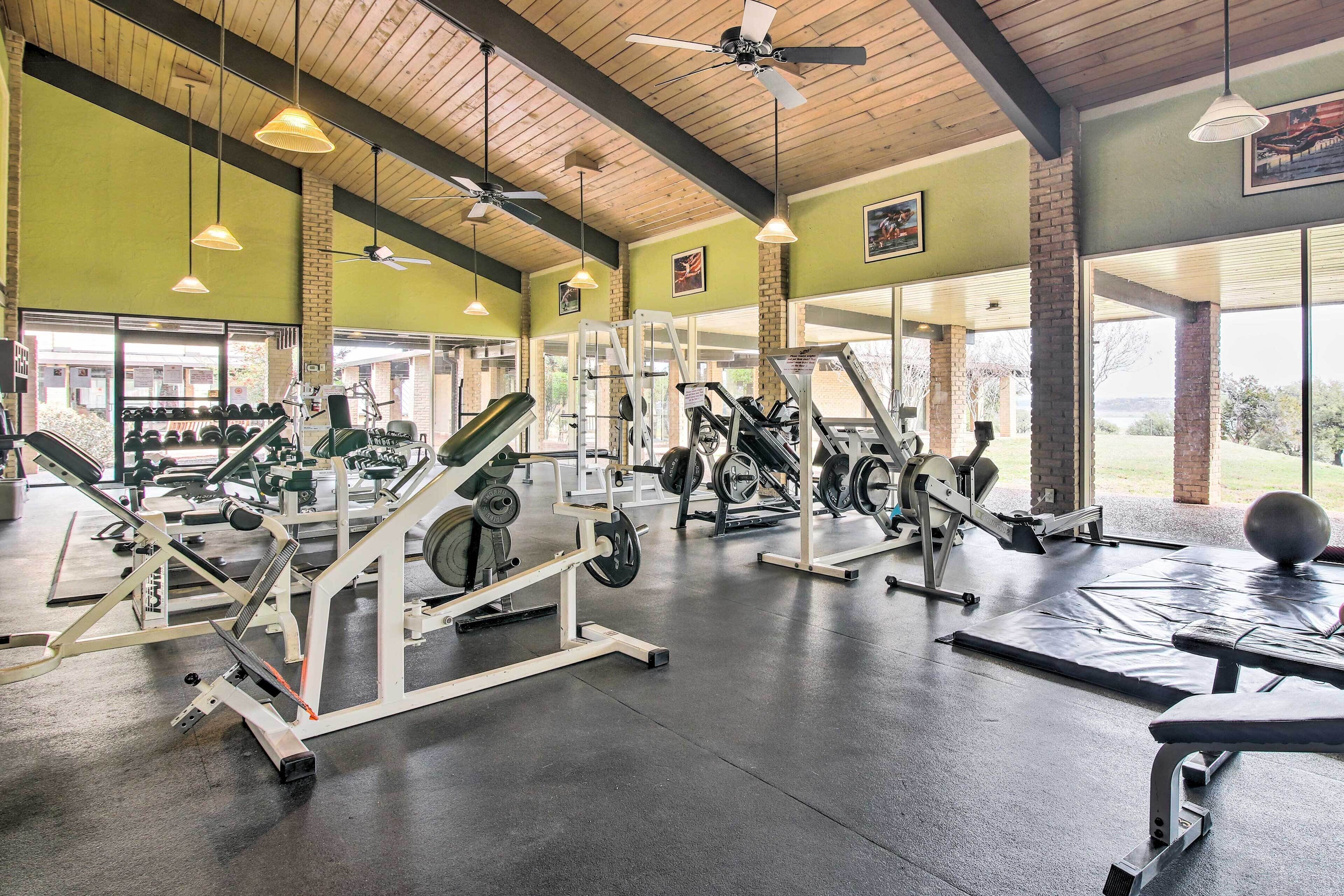 Une salle de sport équipée de divers appareils d’exercice, dotée de grandes fenêtres et d’un ventilateur de plafond.