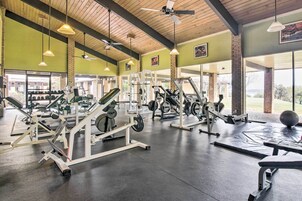 Un gimnasio con diverso equipamiento de ejercicio, ventanas amplias y un ventilador de techo.