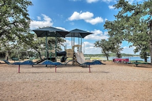 Ein Spielplatz mit Rutschen und Schaukeln, umgeben von Bäumen und einem Gewässer.