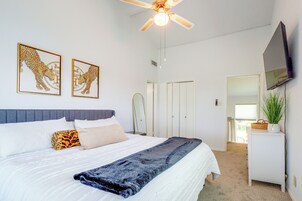 Quarto com uma cama, um ventilador de teto, uma TV e obras de arte na parede.