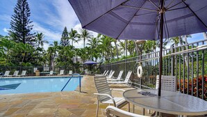 A poolside area with a stone-tiled floor, lounge chairs, a table, and umbrellas. - 1 Mi to Makaha Beach: 10th-floor Condo w/ Views (Waianae)