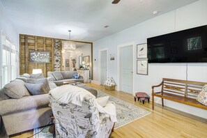 Ein Wohnzimmer mit einer Couch, einem gemusterten Sessel, einer Holzbank, einem Fernseher und einer Wand mit gerahmten Bildern.