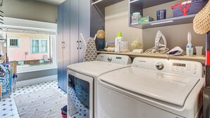 A laundry area with two front-loading washing machines, a drying rack, and a shelf with various items. - Walk to Gulfport Beach! Quiet Home w/ Yard (Gulfport)