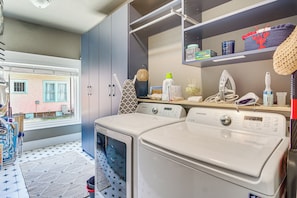 A laundry area with two front-loading washing machines, a drying rack, and a shelf with various items. - Walk to Gulfport Beach! Quiet Home w/ Yard (Gulfport)