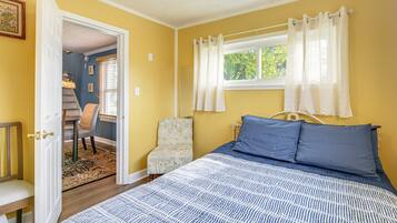 A bedroom with a bed, a chair, a desk, and a window with curtains.