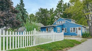 A blue house with a white picket fence, surrounded by greenery and trees.
