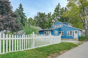 A blue house with a white picket fence, surrounded by greenery and trees.