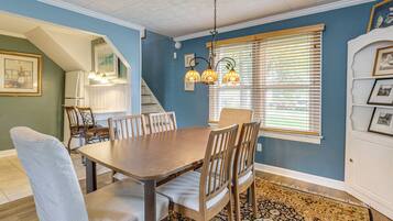 A dining area with a wooden table and chairs, a chandelier, and a window with blinds.