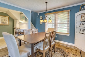 A dining area with a wooden table and chairs, a chandelier, and a window with blinds.