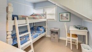 Ein Kinderstockbett mit Schreibtisch und Stuhl, ein Fenster mit Jalousien und ein gerahmtes Bild an der Wand.
