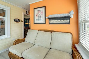 A room with a wicker sofa, a framed picture, and a small shelf with a stuffed toy.