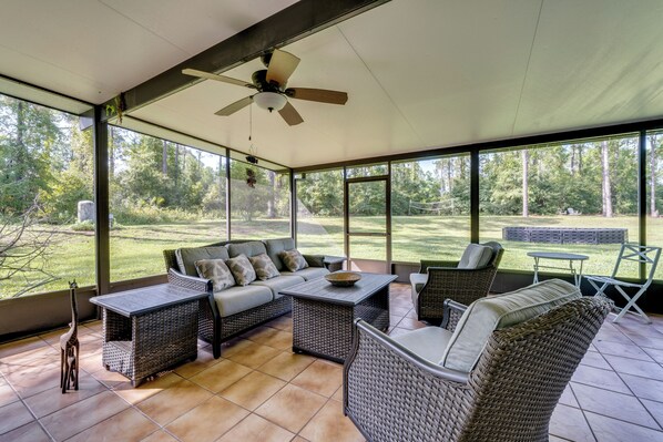 A covered outdoor seating area with wicker furniture, a ceiling fan, and a view of a grassy yard.