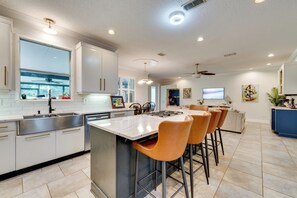 A modern kitchen with a large island, bar stools, and a dining area with a sofa and chairs.