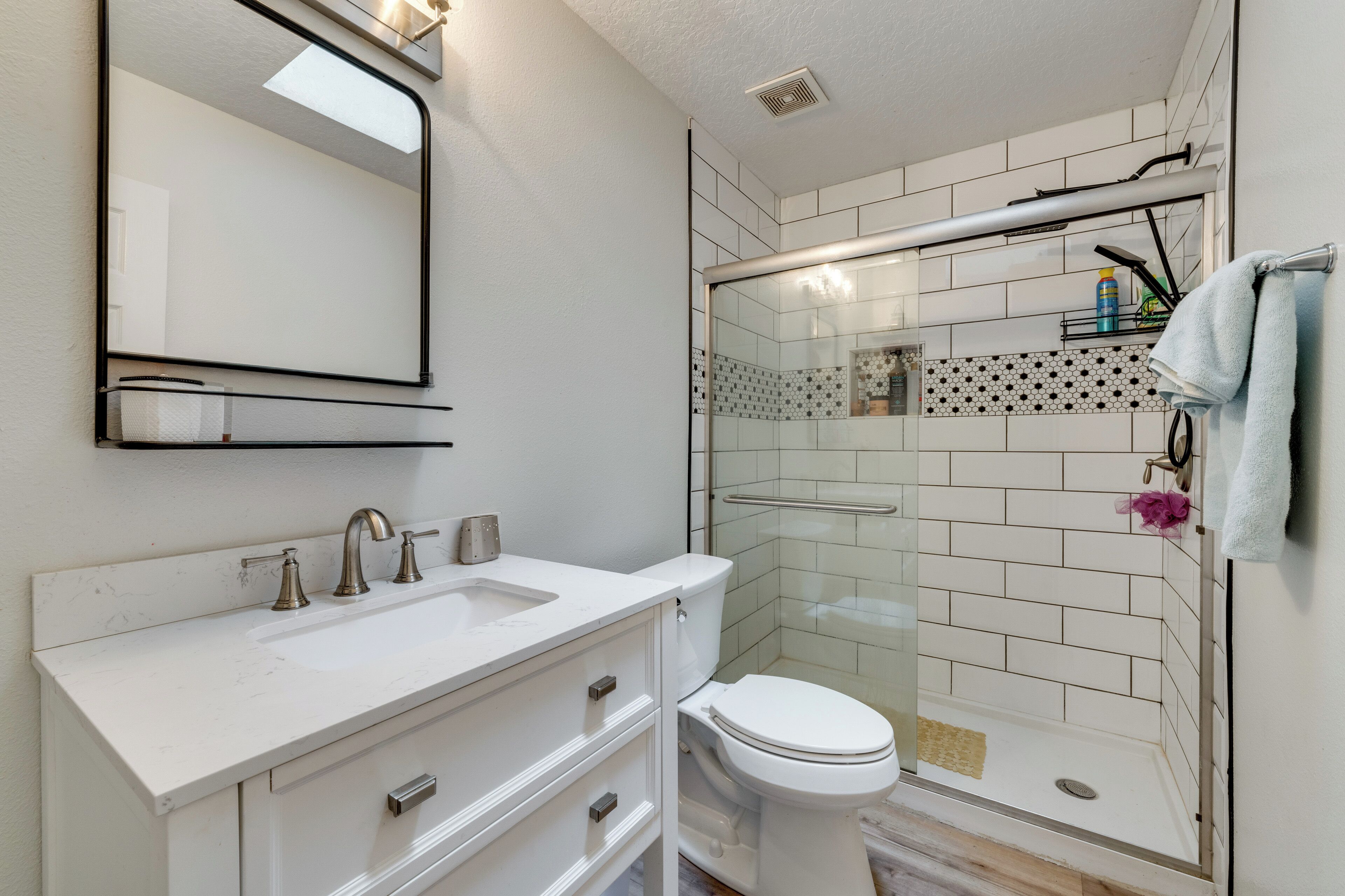 Et badeværelse med en hvid vask, toilet og en brusekabine med glas.