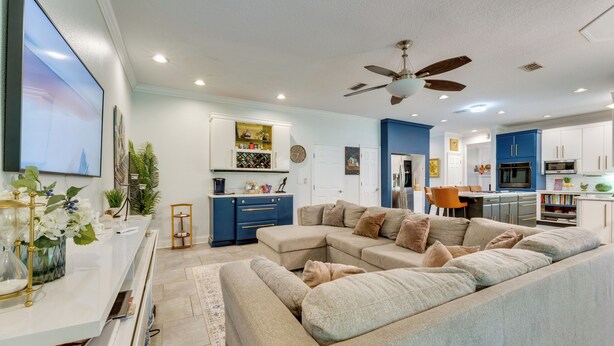 A modern living room with a sectional sofa, a flat-screen TV, and a dining area with a table and chairs. - Pool, Patio + Game Room! Secluded Montverde Home (Montverde)