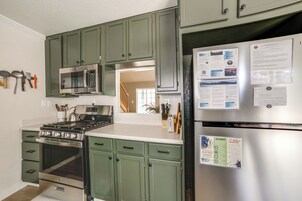 Una cocina con electrodomésticos de acero inoxidable, armarios verdes y un refrigerador con un tablón de anuncios.