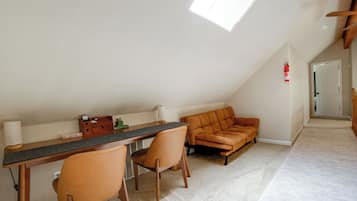 A room with a sloped ceiling, a desk with chairs, a sofa, and a fire extinguisher on the wall.