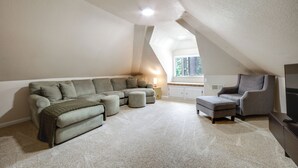 Um quarto estilo loft com sofá seccional, pufes, uma mesa pequena e uma televisão.
