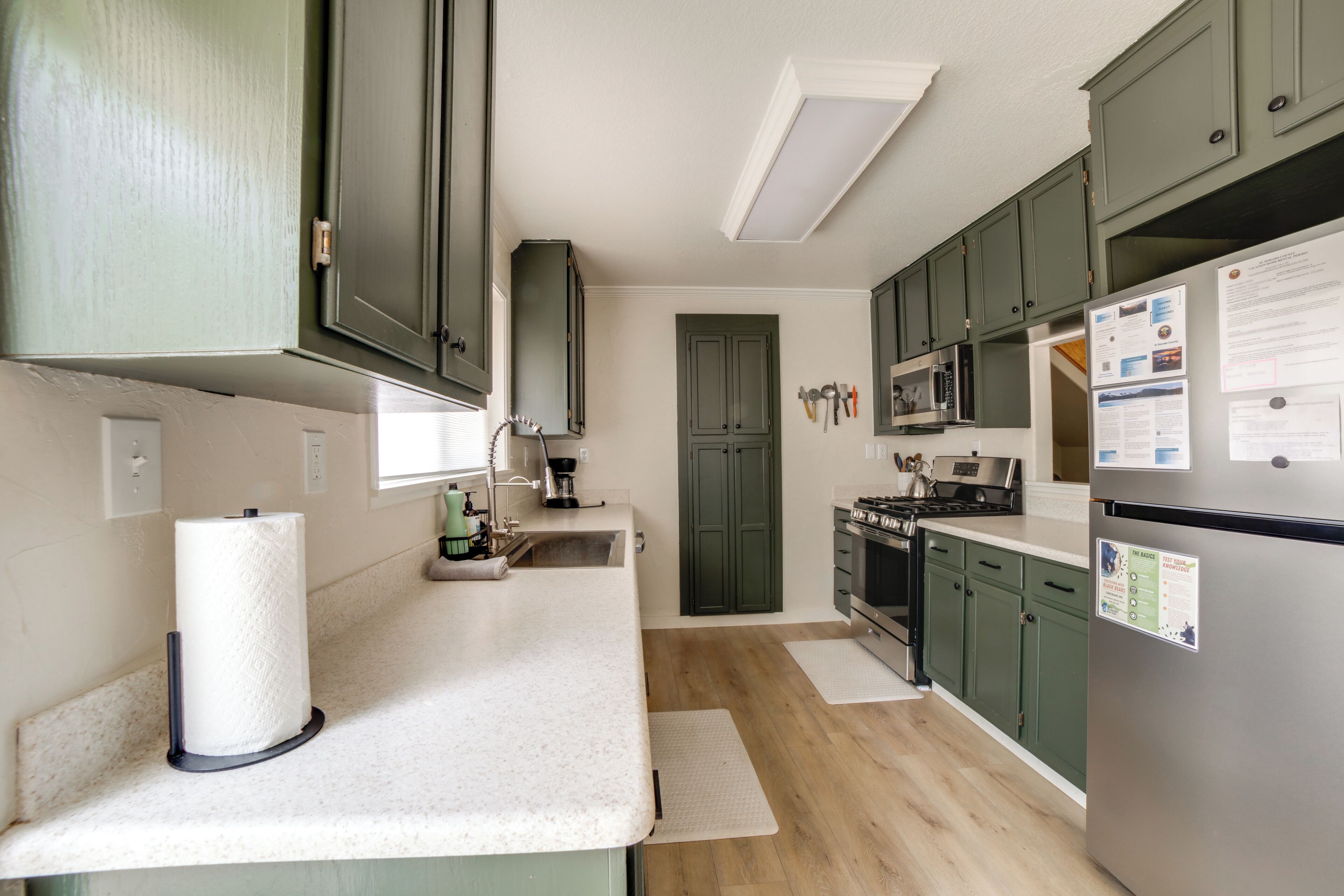 A modern kitchen with green cabinets, stainless steel appliances, and a white countertop.