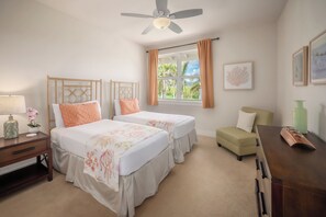 Ein Hotelzimmer mit zwei Betten, einem Schreibtisch, einem Stuhl, einem Vorhangfenster und einem Deckenventilator.
