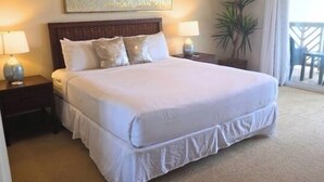 Ett hotellrum med en stor säng, två sängbord med lampor, en takfläkt, ett stort fönster med gardiner och en krukväxt.