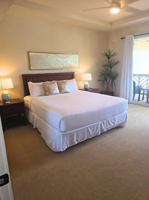 Une chambre d’hôtel avec un grand lit, deux tables de chevet avec des lampes, un ventilateur de plafond, une grande fenêtre avec des rideaux et une plante en pot.