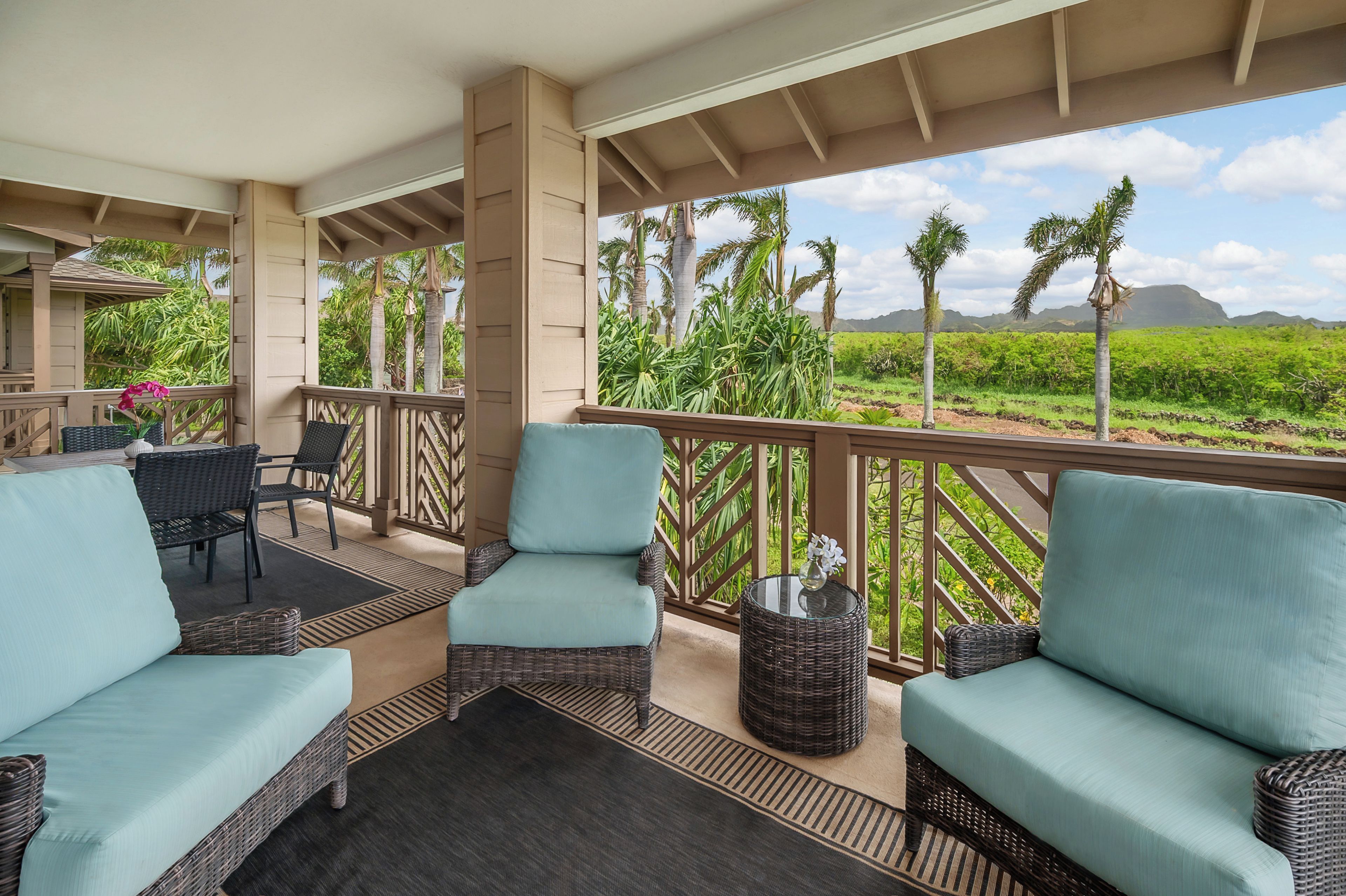 A covered outdoor seating area with wicker furniture and a view of a lush landscape.