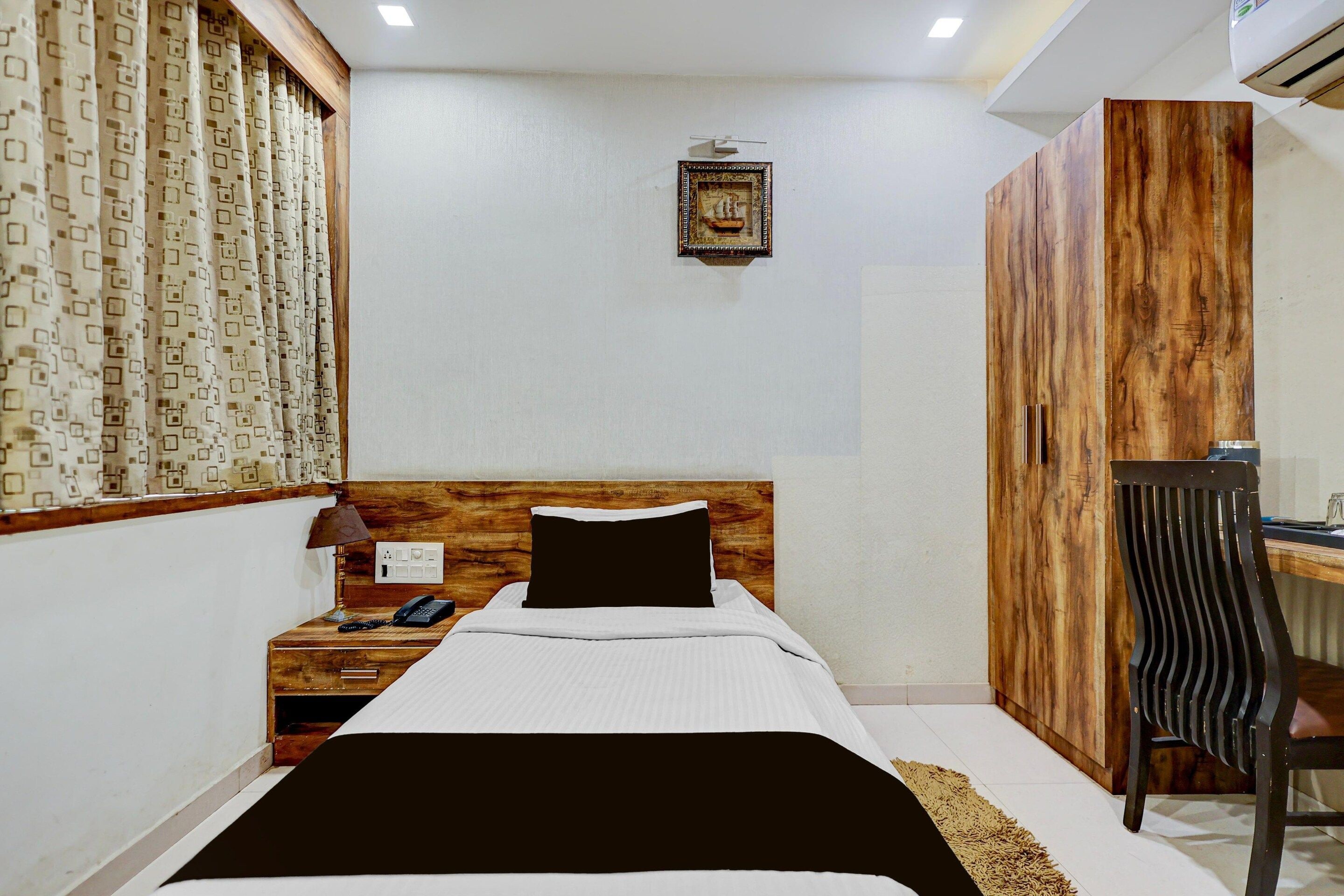 Un dormitorio con cabecera de madera, cama con ropa de cama blanca, mesita de noche con lámpara, escritorio y armario.