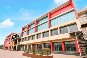 Un edificio de varios pisos con un diseño arquitectónico moderno, que destaca por su llamativo esquema de color rojo y beige y grandes ventanales.