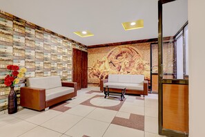 A reception area with two sofas, a vase with flowers, and a decorative wall with a mural. - Palette Mundra Formerly (Mundra)