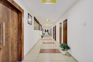 Un couloir d’hôtel avec des portes en bois, des œuvres d’art encadrées, des plantes en pot et un sol carrelé.