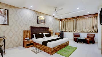 A hotel room with a large bed, a desk, a chair, a ceiling fan, and a window with curtains.