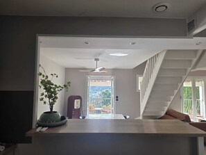 Uma cozinha moderna com uma ilha central, uma área de refeições com cadeiras, uma escadaria e vista para o exterior.