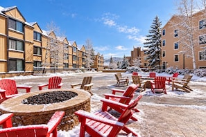 A snow-covered outdoor seating area with red Adirondack chairs and a stone fire pit. - King Bed Studio, Free Shuttle to Slopes & Main Street - Moose Mgmt 425 (Park City)