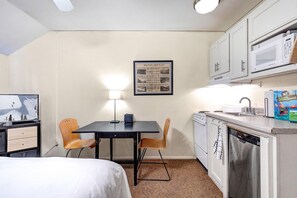 Une chambre d’hôtel compacte comprenant un lit, une petite table à manger avec des chaises, une kitchenette équipée d’un four à micro-ondes et un tableau encadré au mur.