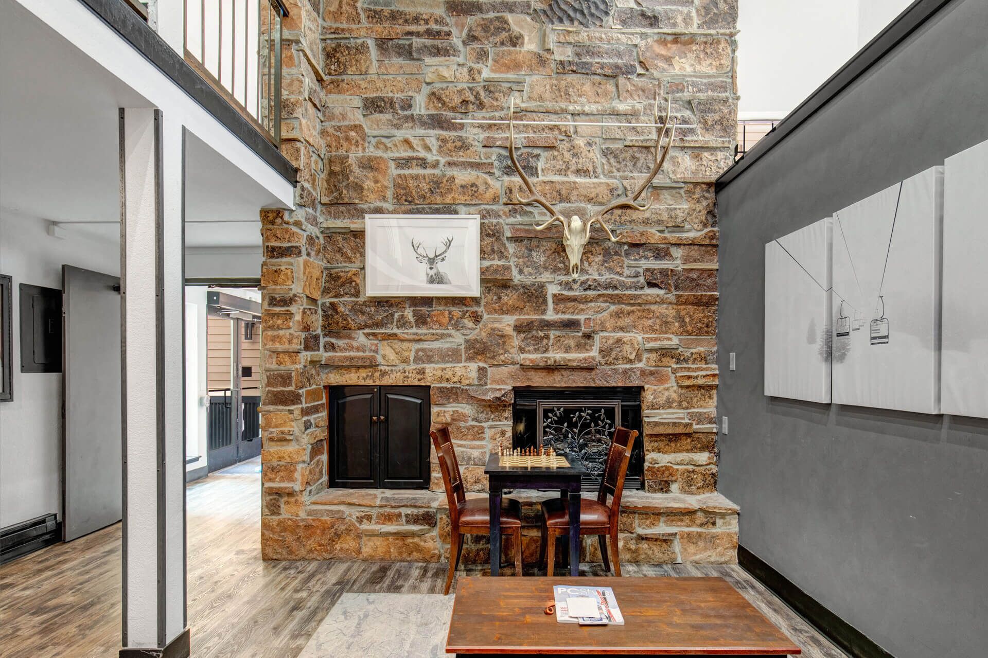 A stone fireplace with a deer skull and antlers decoration, a chessboard, and a table with magazines.