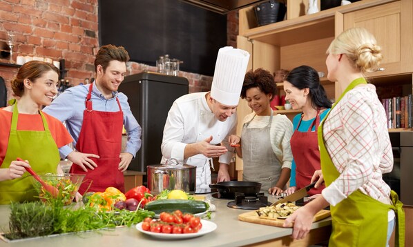 A group of people in a kitchen with a brick wall, a blackboard, and various cooking utensils and ingredients on the counter. - Perseus Apartment near the Colosseum – A stylish stay in the heart of Rome (Roma)
