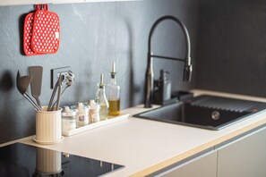 Eine moderne Küche mit einem schwarzen Wasserhahn, einem roten Topflappen und Besteck in einem weißen Behälter.