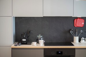A kitchen with a coffee maker, a mug, a kettle, and a red polka-dotted pot holder on the counter. - Perseus Apartment near the Colosseum – A stylish stay in the heart of Rome (Roma)