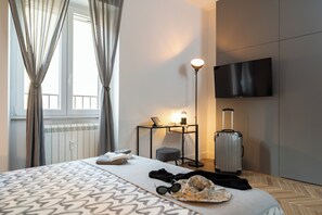 A hotel room with a bed, a bedside table with a lamp, a suitcase, and a TV on the wall. - Perseus Apartment near the Colosseum – A stylish stay in the heart of Rome (Roma)