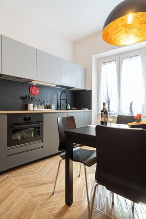 Eine moderne Küche mit grauen Schränken, einem eingebauten Backofen und einem Essbereich mit Tisch und Stühlen.