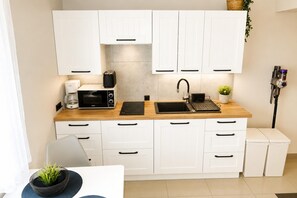 A modern kitchen with white cabinets, a wooden countertop, a built-in microwave, a coffee maker, a toaster, a sink with a faucet, and a small potted plant. - Studio for 4 People, Close to the sea (Kamien Pomorski)