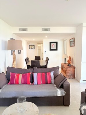 A living room with a sofa, a dining table with chairs, a lamp, and a decorative piece on a wooden cabinet. - Unique in St Cyprien, right on the water (Saint-Cyprien)
