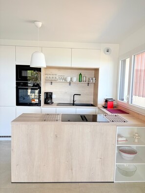 A modern kitchen with a central island, a built-in oven, and a coffee machine. - Unique in St Cyprien, right on the water (Saint-Cyprien)